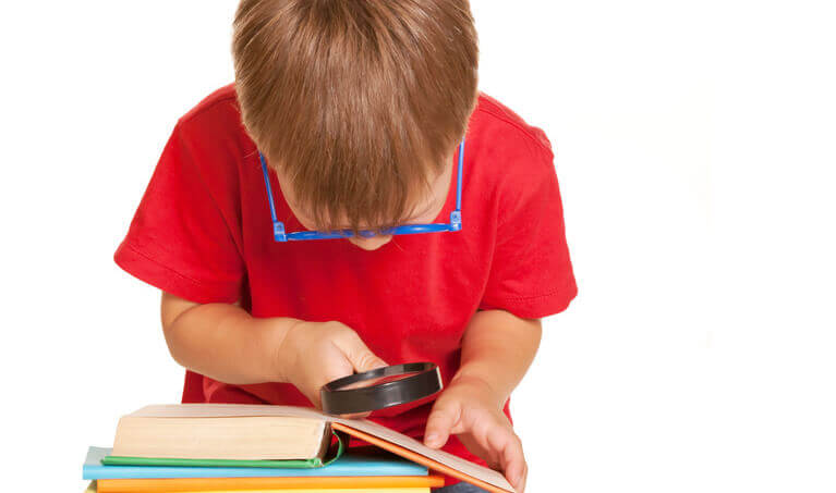 Child using a magnifying glass to read a book